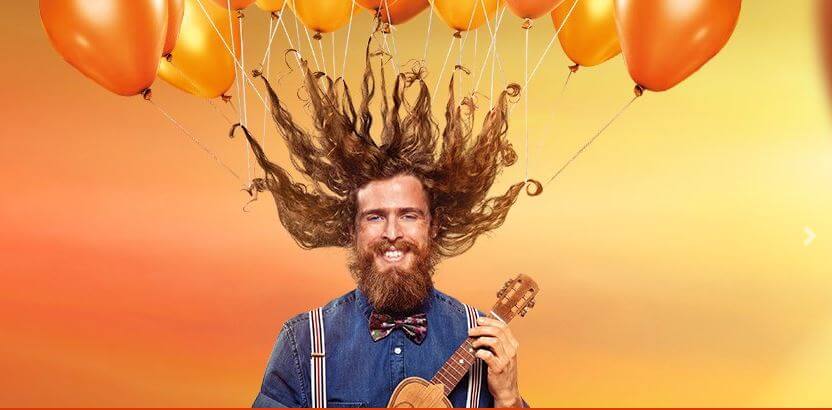 Imagem publicitária Bacana Play: Homem sorridente com vários balões laranja presos ao cabelo comprido